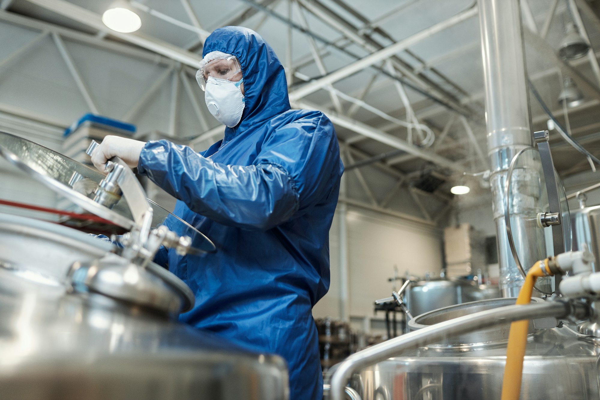 Man wearing protective gear opening tank at chemical plant or factory